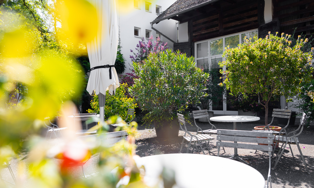 Terasse mit kleinen Tischen und Stühlen, verschwommene Blüten im Bildvordergrund