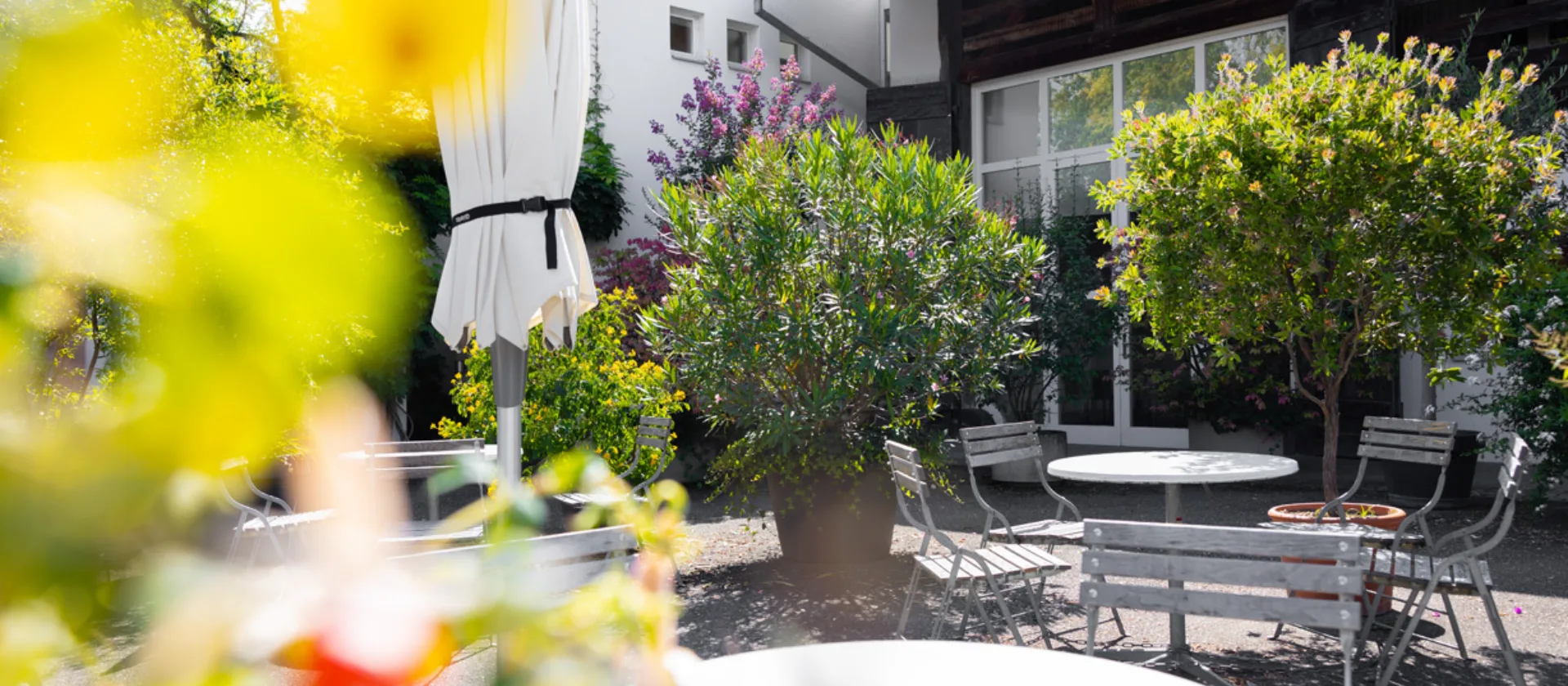 Terasse mit kleinen Tischen und Stühlen, verschwommene Blüten im Bildvordergrund